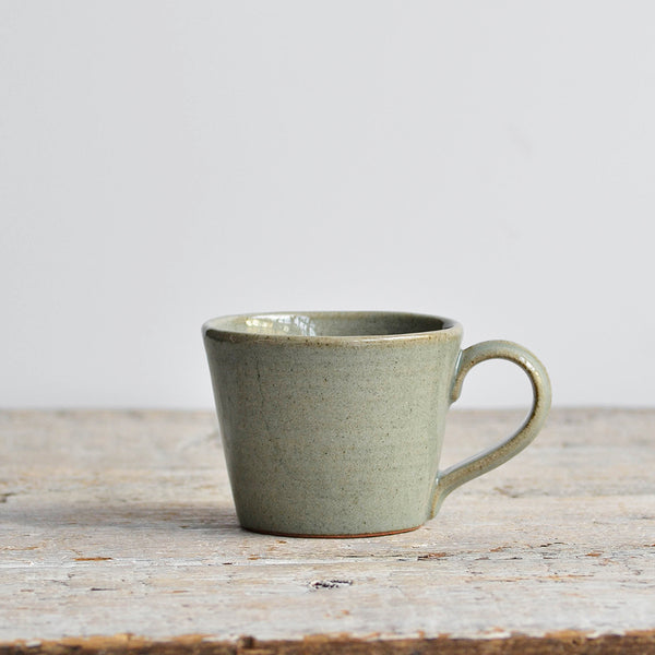 Green ceramic mug on a wooden surface with a light gray background - Nom Living