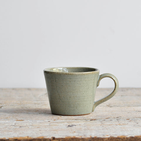 Green ceramic mug on a wooden surface with a light gray background - Nom Living