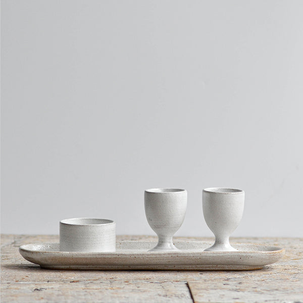 Minimalist snow white ceramic breakfast set including an oval tray, two egg cups, and a mini condiment ramekin. Nom Living