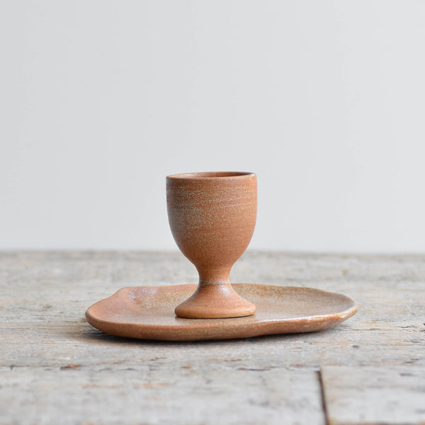 Earthy rust-glazed ceramic egg cup with an teardrop side tray