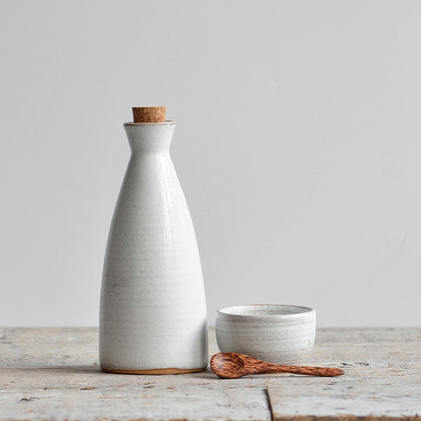 Minimalist snow-white ceramic oil pouring bottle next to a small stoneware salt condiment bowl with a tiny wooden spoon. Nom Living