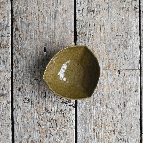 Hand-moulded dark green stoneware bowl in an organic triangular shape with a textured, earthy glaze, designed for serving olives, dips, and small appetizers. placed in a wood table