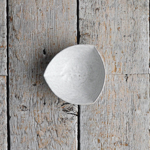 Hand-moulded Snow-White stoneware bowl in a soft, irregular triangular shape with a textured surface, ideal for serving olives, dips, and side dishes placed on a wood table.