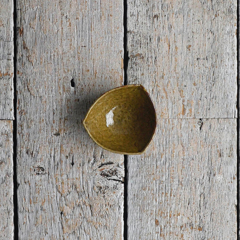 Mini hand-shaped stoneware bowl for individual condiments, featuring a soft triangular silhouette and a textured deep green glaze. Placed in a wood table